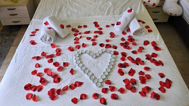 A bed with rose petals and a heart-shaped arrangement of candles.
