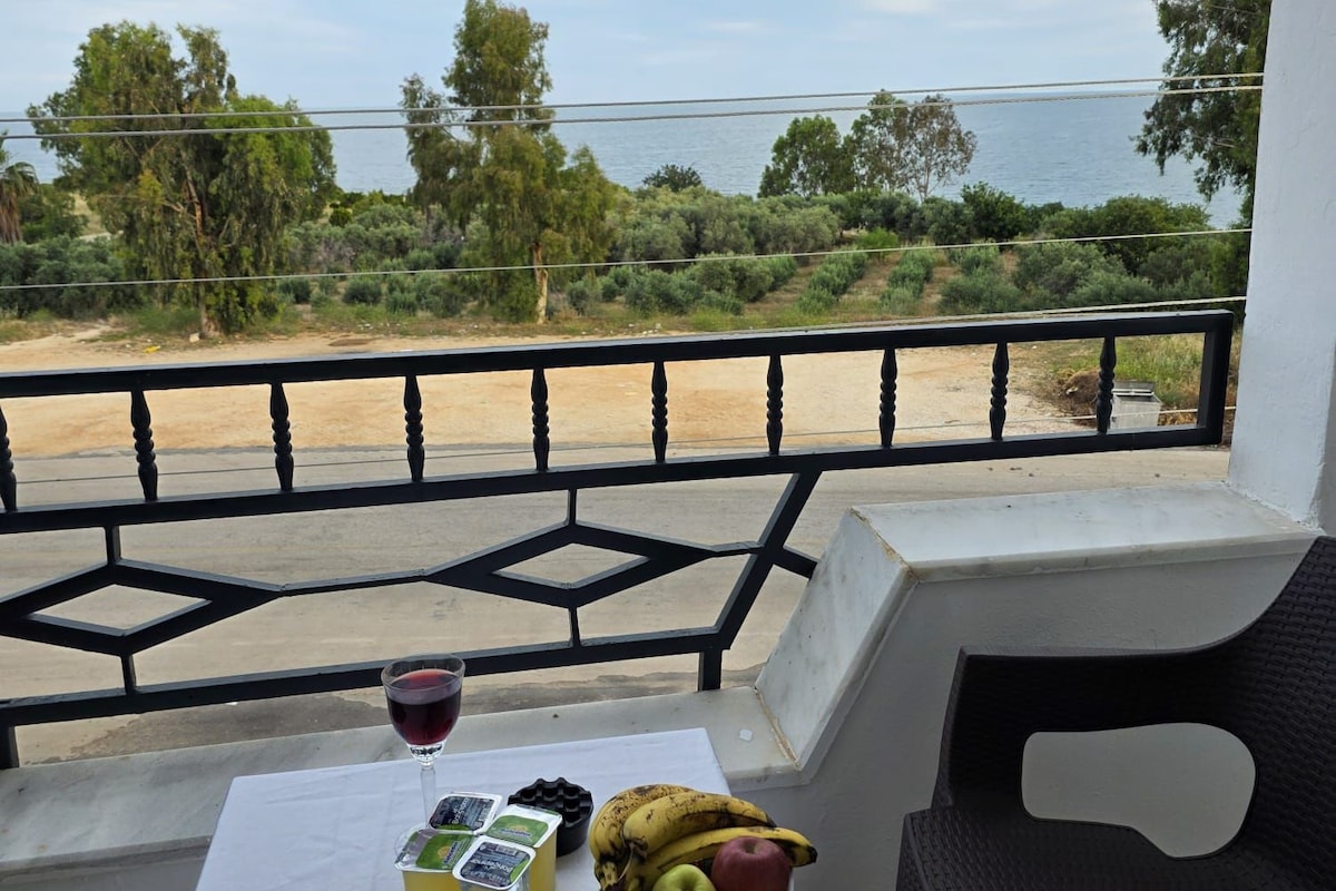 A balcony with a table set for a meal, a candle, and a view of the sea and greenery.