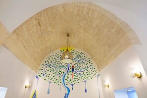 Une pièce dotée d’un plafond au design original, d’un luminaire suspendu et d’appliques murales.