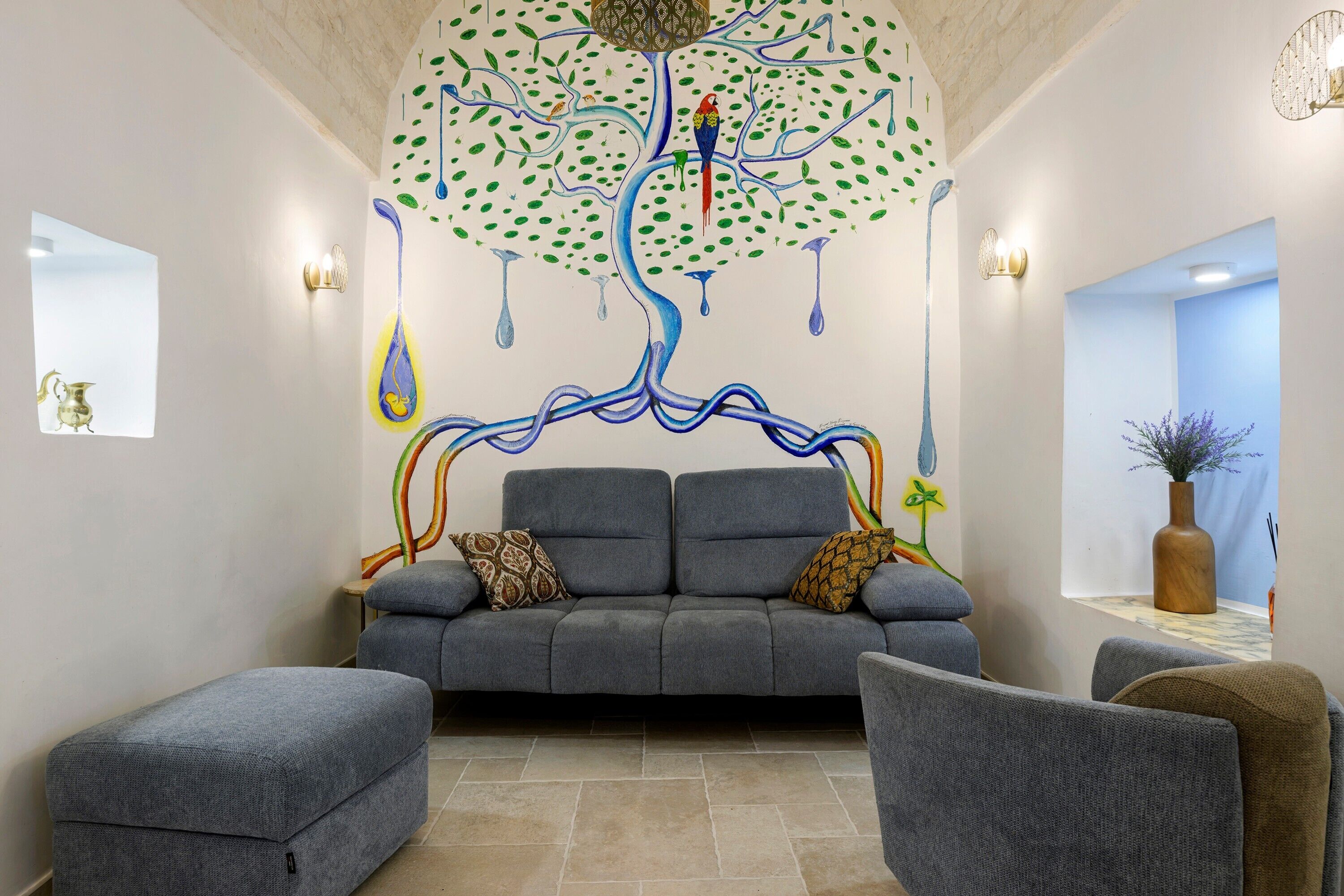 Un salon moderne avec un canapé gris, deux fauteuils et une fresque murale décorative.