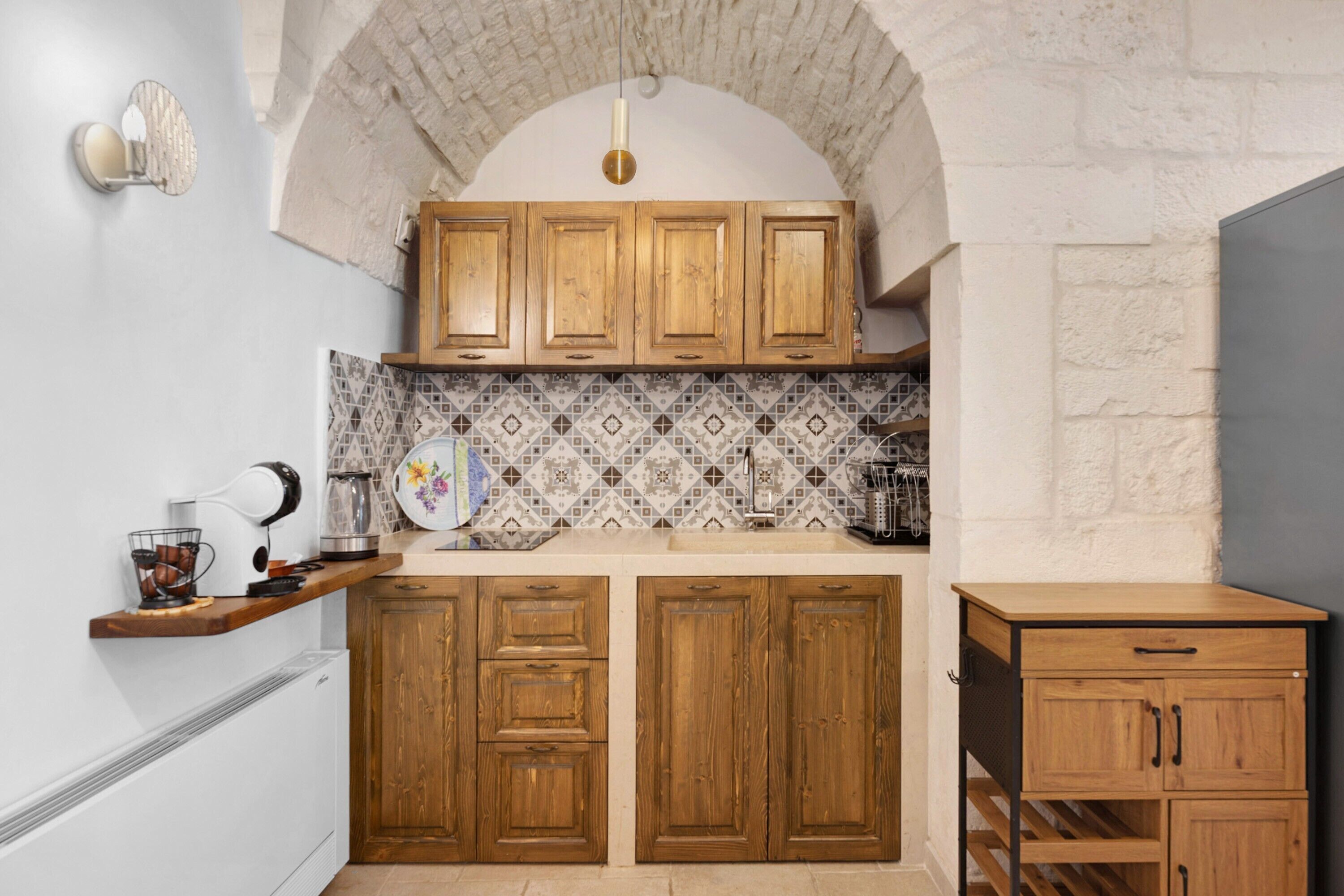 Une cuisine avec des meubles de rangement en bois, un dosseret décoré et un luminaire suspendu.