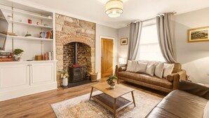 A living room with a stone fireplace, a leather sofa, a coffee table, and a bookshelf. - The Old Forge - North East Escapes (Warkworth)