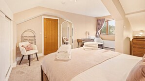 A bedroom with a large bed, a chair, a desk, and a window with curtains. - The Old Forge - North East Escapes (Warkworth)