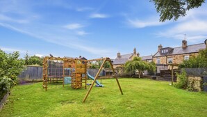 A backyard with a wooden play structure, a swing set, and a slide. - The Old Forge - North East Escapes (Warkworth)