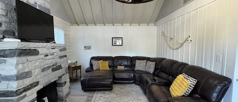 A living room with a stone fireplace, a leather sectional sofa, and a patterned rug.