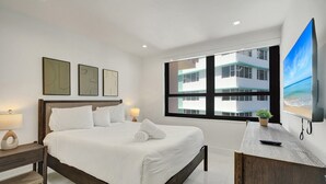A modern hotel room with a large bed, a flat-screen TV, and a view of a building through the window. - Bay & Ocean View 4 BDR Spacious Condo Resort Amenities 1616 (Miami Beach)