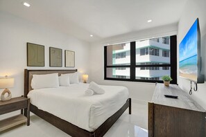 A modern hotel room with a large bed, a flat-screen TV, and a view of a building through the window. - Bay & Ocean View 4 BDR Spacious Condo Resort Amenities 1616 (Miami Beach)