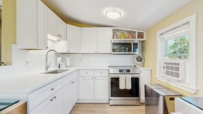 A modern kitchen with white cabinetry, stainless steel appliances, and a window providing natural light. - Walk to the Beach From This East End Retreat (Provincetown)
