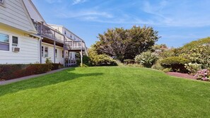 Ein Wohnhaus mit gepflegtem Rasen, einer Veranda mit Geländer und einem großen Baum im Hintergrund.