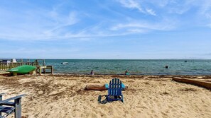Une plage avec une jetée en bois, un fauteuil de jardin vert et une chaise Adirondack bleue.