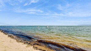 A beach with clear water, a boat in the distance, and a sandy shore. - Walk to the Beach From This East End Retreat (Provincetown)
