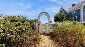 A gated entrance with a white picket fence, leading to a house with a dark exterior and a visible chimney. - Walk to the Beach From This East End Retreat (Provincetown)
