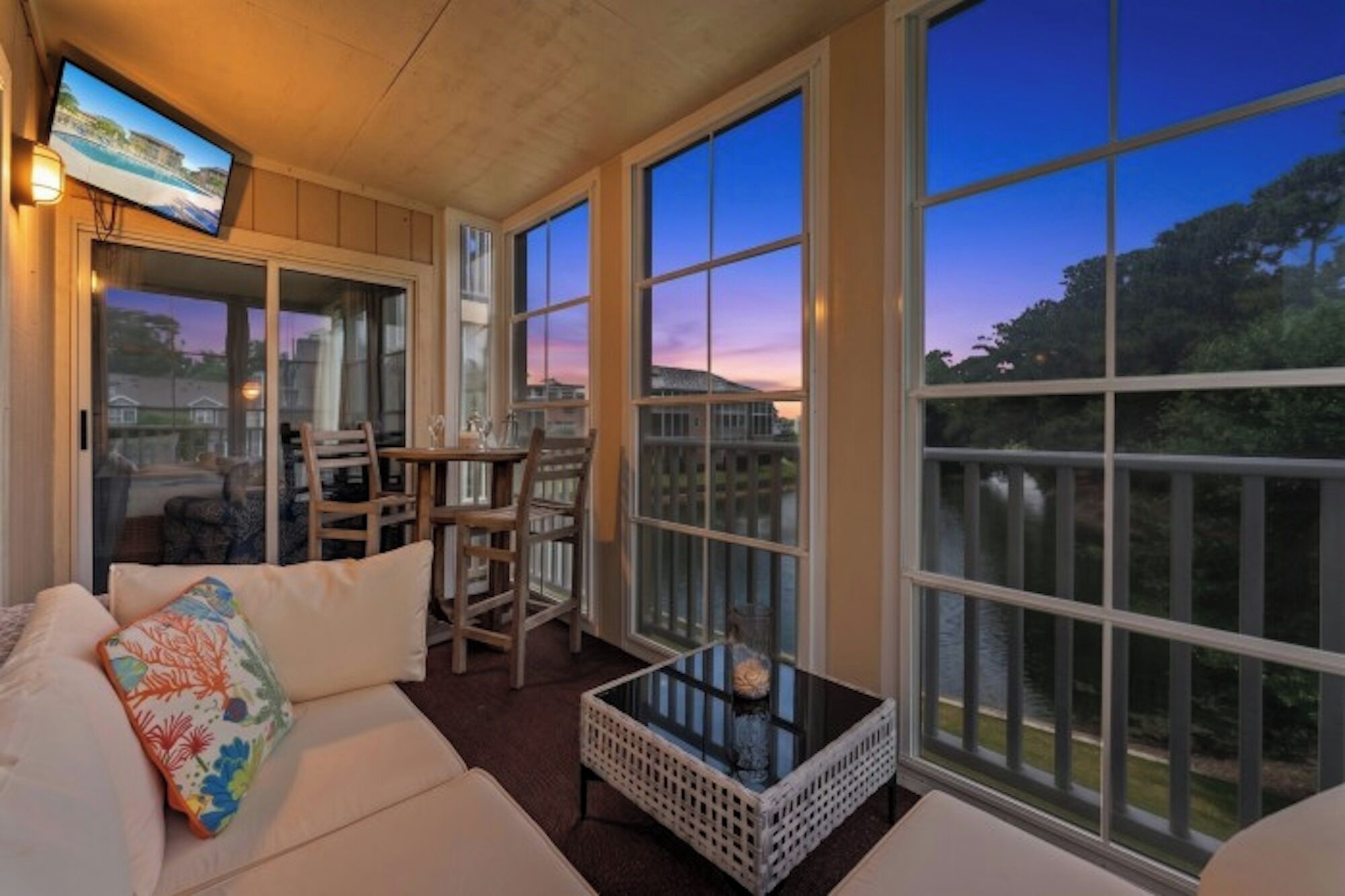 A sunroom with a sofa, chairs, a table, and large windows.