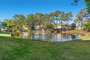 Ein Golfplatz mit Teich, Bäumen und Häusern im Hintergrund.
