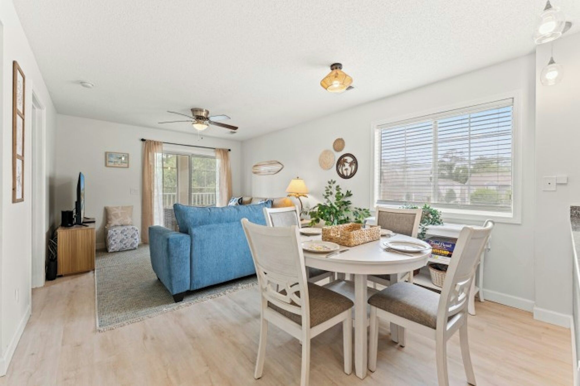 A living room with a sofa, dining table, chairs, a ceiling fan, and a window with blinds.
