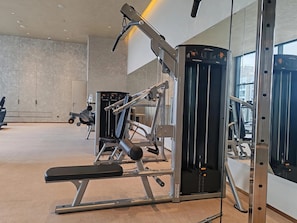 Ein Fitnessraum mit verschiedenen Trainingsgeräten, einer Bank und einer Spiegelwand.