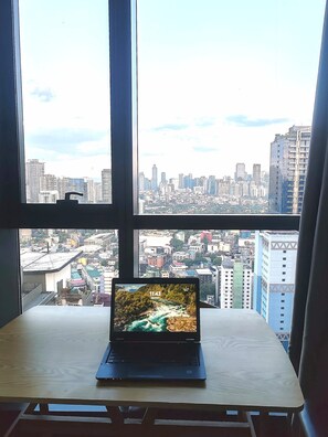 Ein Laptop auf einem Tisch, durch große Fenster ist ein Stadtblick zu sehen.
