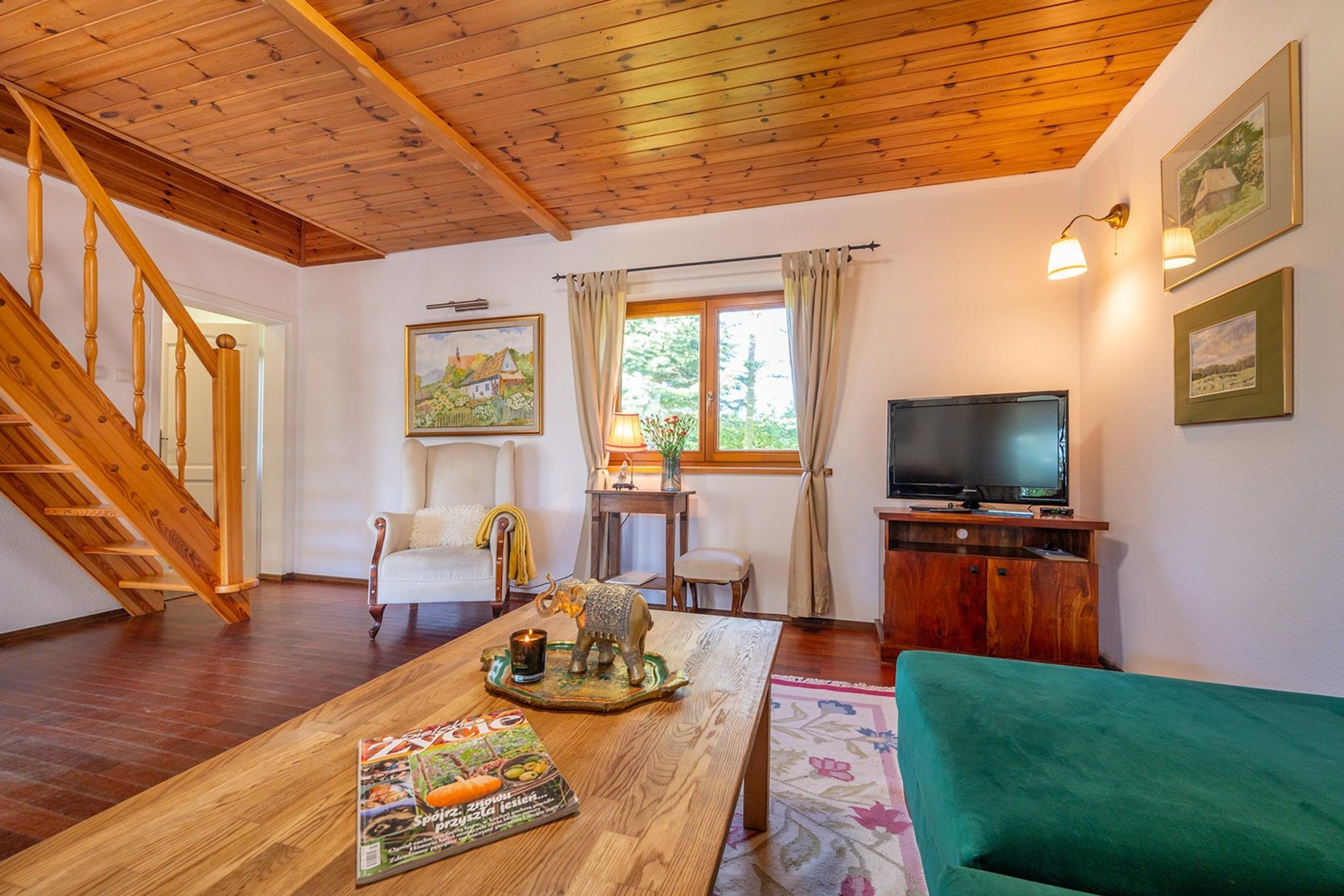 A cozy living room with a wooden staircase, a television, a dining table with a magazine, and a green sofa.
