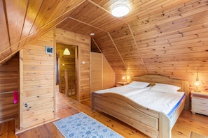 A wooden room with a sloped ceiling, a bed with white bedding, a nightstand, and a small table. - Comfortable holiday home with a fireplace, Bobolin (Bobolin)