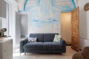 Een kamer met een grijze bank, een muurschildering, een houten deur en een wit kastje.
