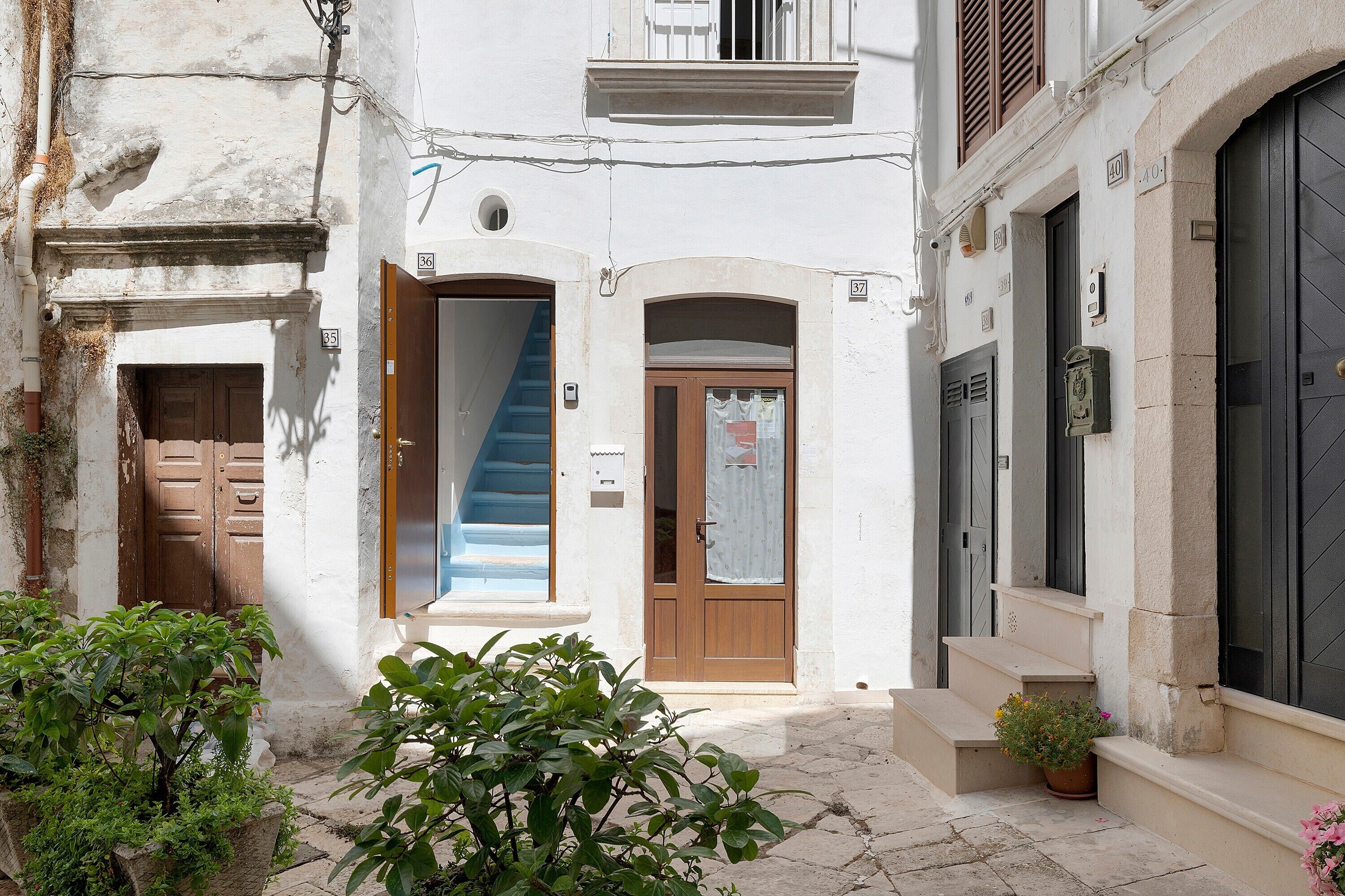 Une rue étroite, avec un immeuble dont la façade présente une porte en bois, un escalier bleu et une porte noire ornée d’une plaque numérotée.