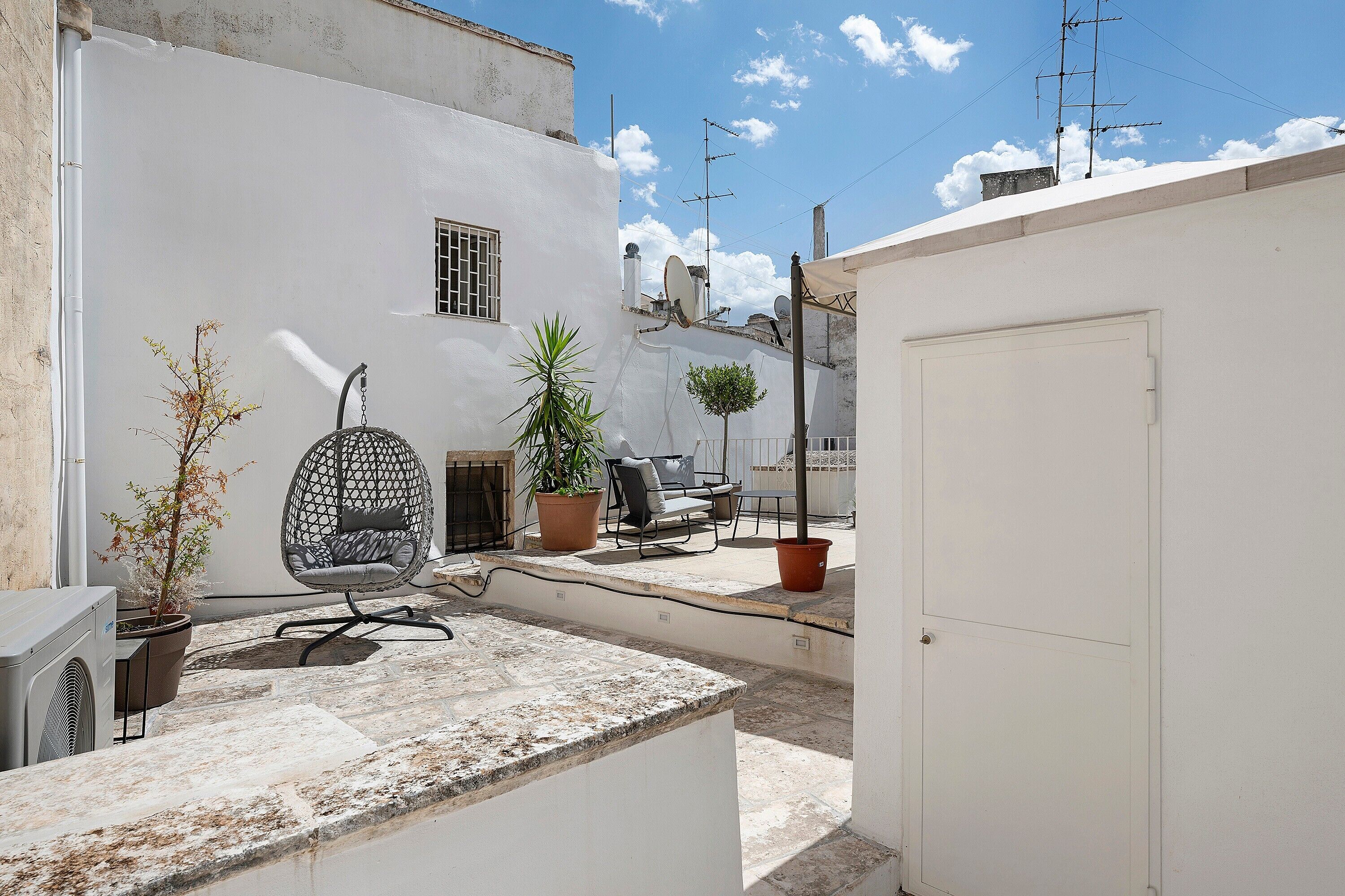 A courtyard with a white building, a hanging chair, a potted plant, and a door.