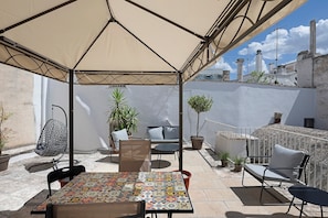 A covered outdoor seating area with a table and chairs, potted plants, and a view of the cityscape. - Apartment 'Casa Itria, Acqua' with Private Terrace, Wi-Fi and Air Conditioning (Martina Franca)