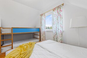 A bedroom with a bunk bed, a single bed, a window with floral curtains, and a bedside lamp. - Large and comfortable holiday home with a terrace (Bobolin)