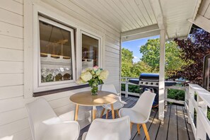 Eine überdachte Veranda mit Tisch, Stühlen, einem Grill und einem Fenster mit Spitzenvorhängen.