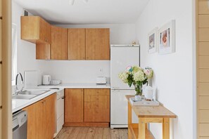 A compact kitchen with wooden cabinets, a white refrigerator, a sink, and a small table with a tray of food and a vase of flowers. - Large and comfortable holiday home with a terrace (Bobolin)