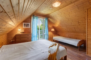 A cozy attic bedroom with a wooden sloped ceiling, a bed, a bench, and a dresser. - Comfortable holiday home with a fireplace (Bobolin)