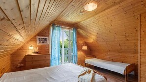 A wooden cabin bedroom with a bunk bed, a bedside table, and a window with curtains. - Comfortable holiday home with a fireplace (Bobolin)