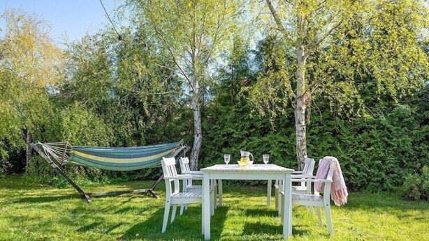 An outdoor seating area with a table and chairs, a hammock, and a hedge in the background. - Comfortable holiday home with a fireplace (Bobolin)