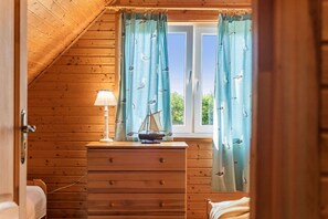 A wooden room with a window, curtains, a lamp, and a dresser with a model ship. - Comfortable holiday home with a fireplace (Bobolin)