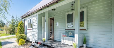 A two-story house with a porch, a covered entryway, and a small garden area with potted plants.