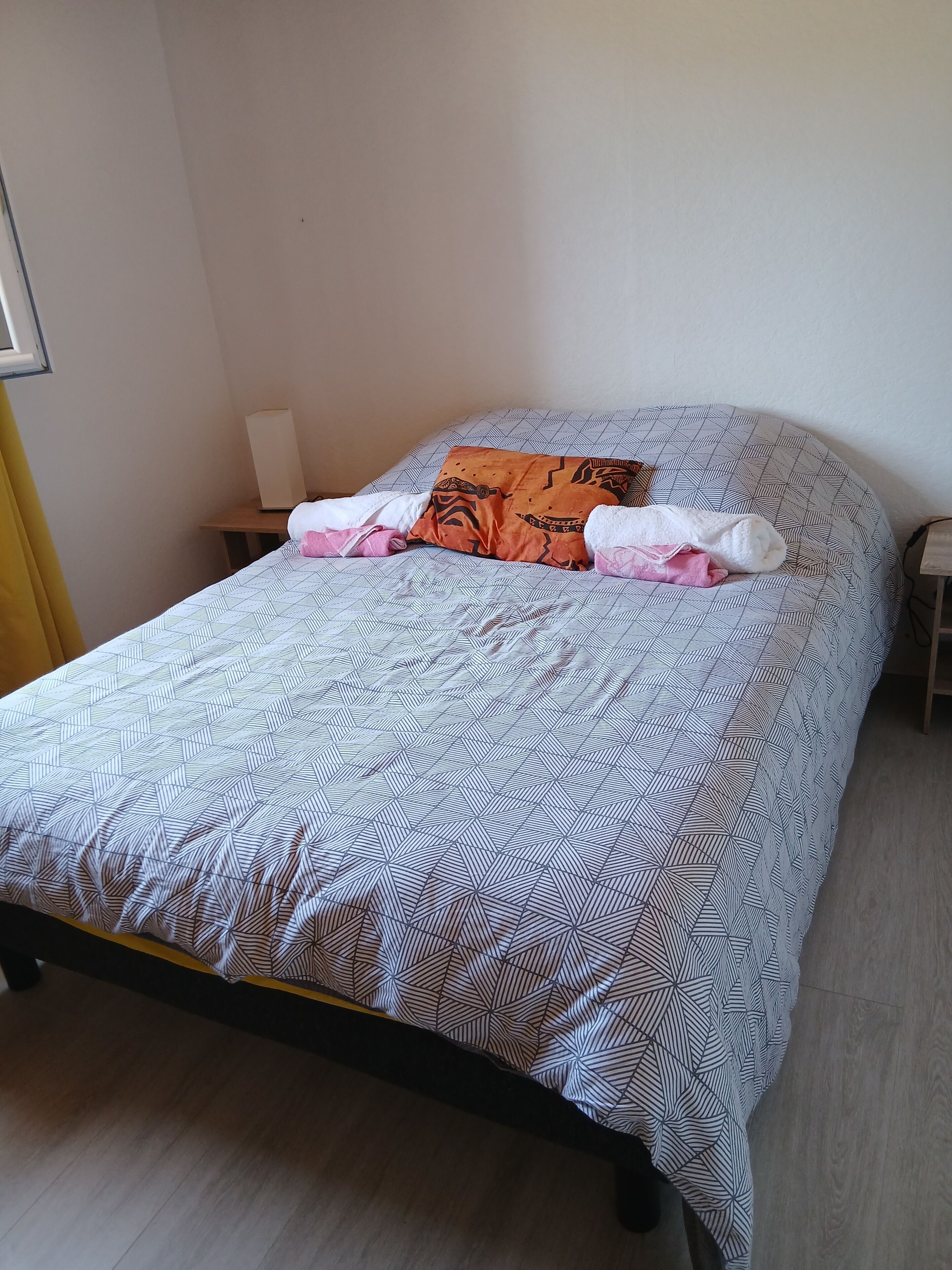 Ein Bett mit einem gemusterten Überwurf, Kissen und einem Nachttisch mit Lampe.