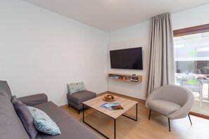 Ein modernes Wohnzimmer mit Sofa, Sessel, Couchtisch und einem an der Wand befestigten Flachbildfernseher.