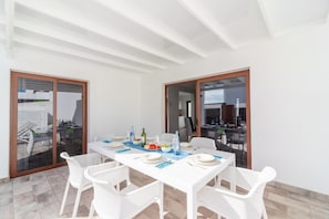 A dining area with a white table set for four, surrounded by white chairs, with a view of the outdoor patio. - Villa Omura 16 - Three Bedroom Villa, Sleeps 6 (Playa Blanca)