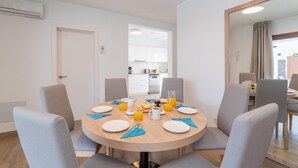 Un comedor con una mesa redonda dispuesta para cuatro personas, con platos, cubiertos y una jarra de jugo de naranja.