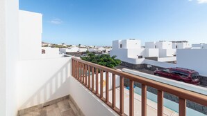 Un balcón con vista a edificios blancos, un vehículo rojo y un cielo azul despejado.
