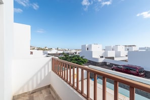 A balcony with a view of white buildings, a red vehicle, and a clear blue sky. - Villa Omura 16 - Three Bedroom Villa, Sleeps 6 (Playa Blanca)