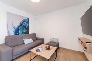 Ein modernes Wohnzimmer mit grauem Sofa, einem kleineren grauen Sessel, einem Couchtisch aus Holz mit Zeitschriften und einem großen abstrakten Gemälde an der Wand.