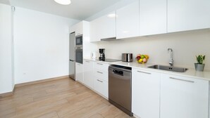Una cocina moderna con armarios blancos, electrodomésticos de acero inoxidable, lavavajillas y un frutero sobre la encimera.