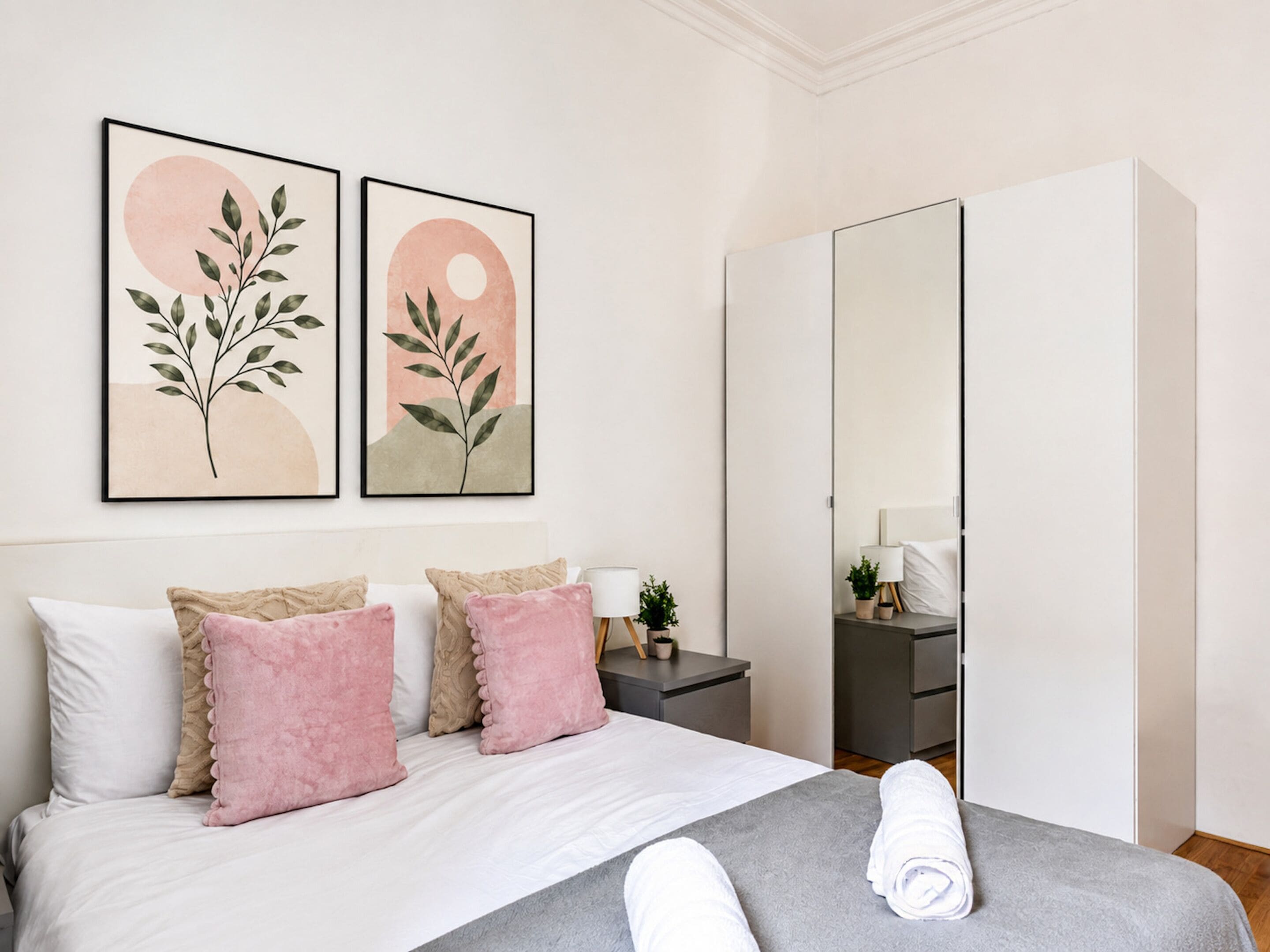 Hotelkamer met een bed, kussens, een nachtkastje, een lamp, een spiegel en twee kunstwerken aan de muur.