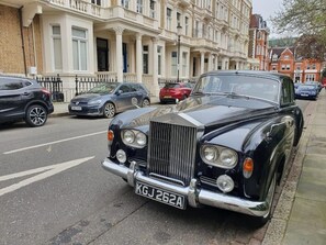 Ein klassischer schwarzer Wagen steht auf einer Straße, im Hintergrund ein Gebäude.