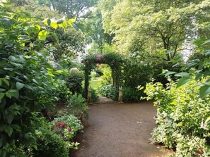 A garden pathway with a wooden archway surrounded by lush greenery and flowering plants. - 2 bedroom Kensington apartment with terrace and usage of large gardens (London)