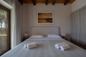 A hotel room with a large bed, two bedside lamps, a painting above the bed, and a view through a window. - Villa Koule - Three Bedroom Villa, Sleeps 6 (Kalami)