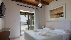 A hotel room with a bed, a TV, a painting, and a view of a pool and landscape. - Villa Koule - Three Bedroom Villa, Sleeps 6 (Kalami)