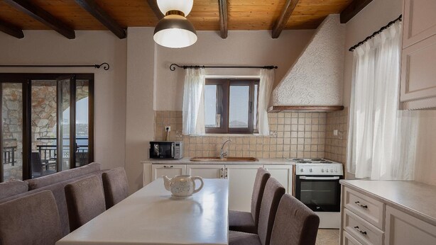 A kitchen with a dining table, chairs, a microwave, a stove, and a window with curtains. - Villa Koule - Three Bedroom Villa, Sleeps 6 (Kalami)