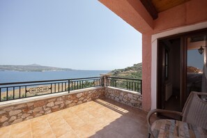 Ein Balkon mit Steinmauer und Metallgeländer mit Blick auf ein Gewässer und eine hügelige Landschaft.
